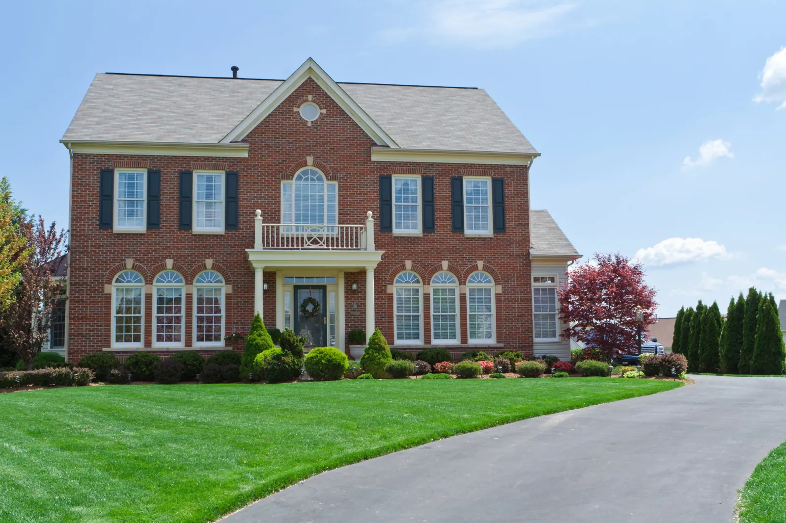 Two-story brick colonial home with black shutters and a landscaped front lawn